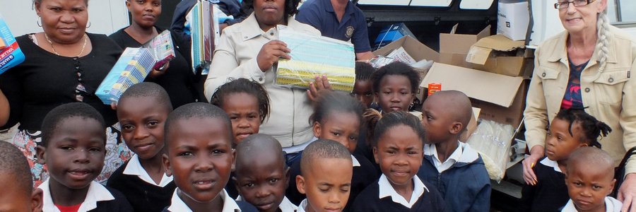 Agter vlnr is Jack Doyle, Nonisokolo Mani (skoolhoof), Malcolm Bury en Anita Doyle saam met leerders tydens die oorhandiging van groot hoeveelhede skryfbenodigdhede aan Masakhane Primary School